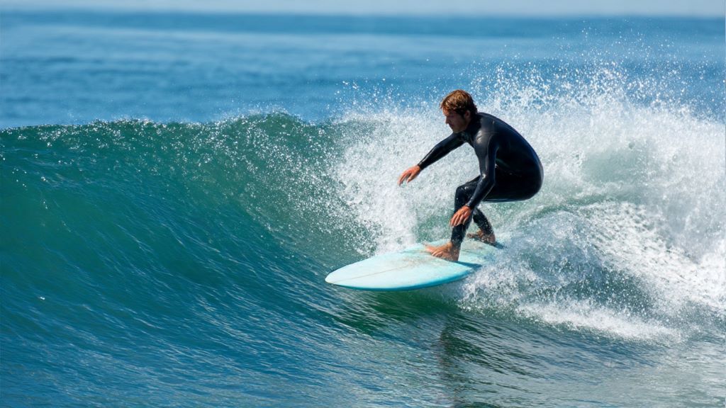 Surfer riding an 8ft egg surfboard on a small blue wave showing smooth turning style and classic technique